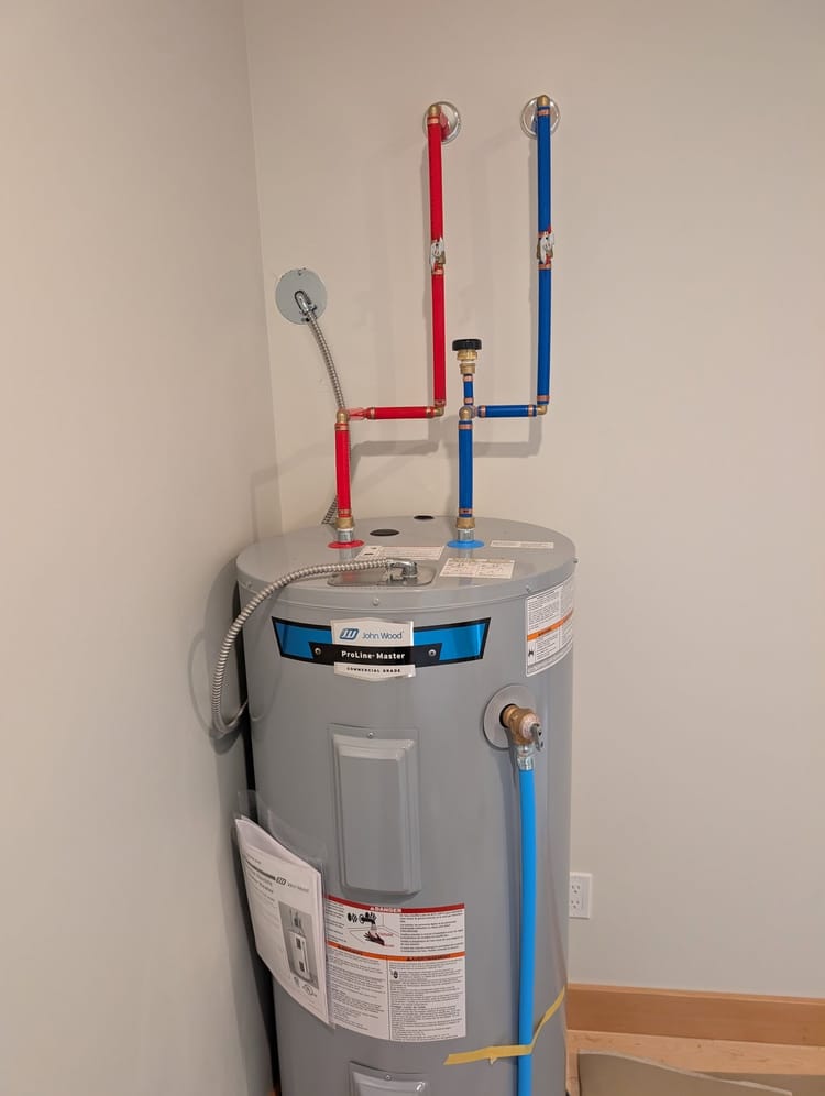 A commercial-grade electric hot water tank installed by KGH Plumbing, with new hot and cold supply lines and a temperature and pressure relief line.